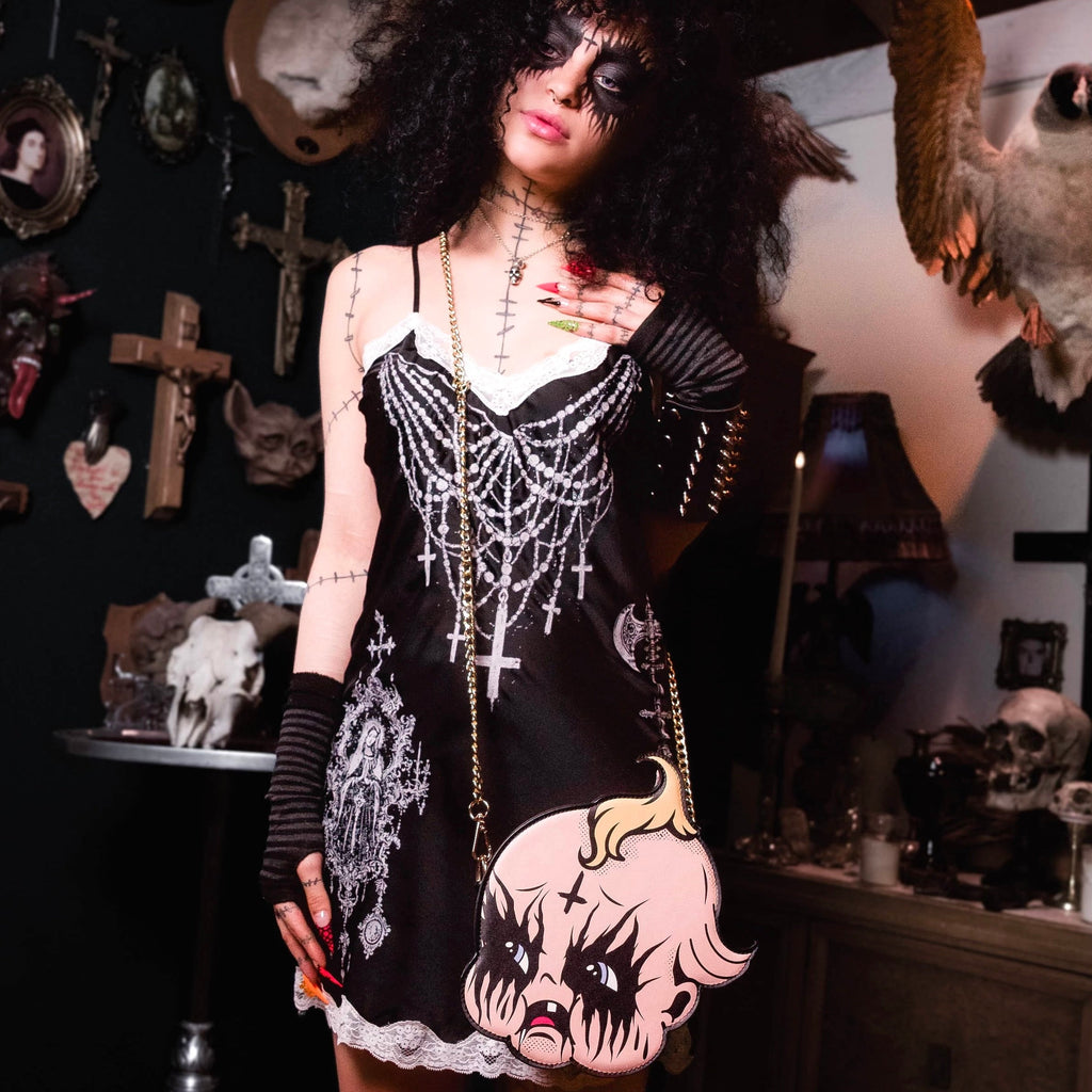 Person in a dark, gothic-style outfit with decorative accessories in a room with dark walls and various decorations.