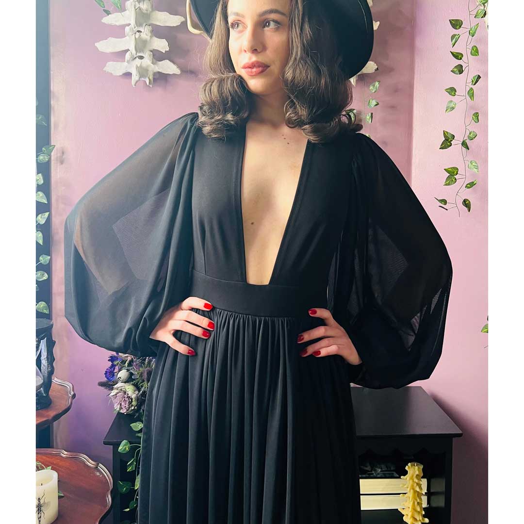 Woman wearing a black dress with sheer sleeves in a decorative setting.