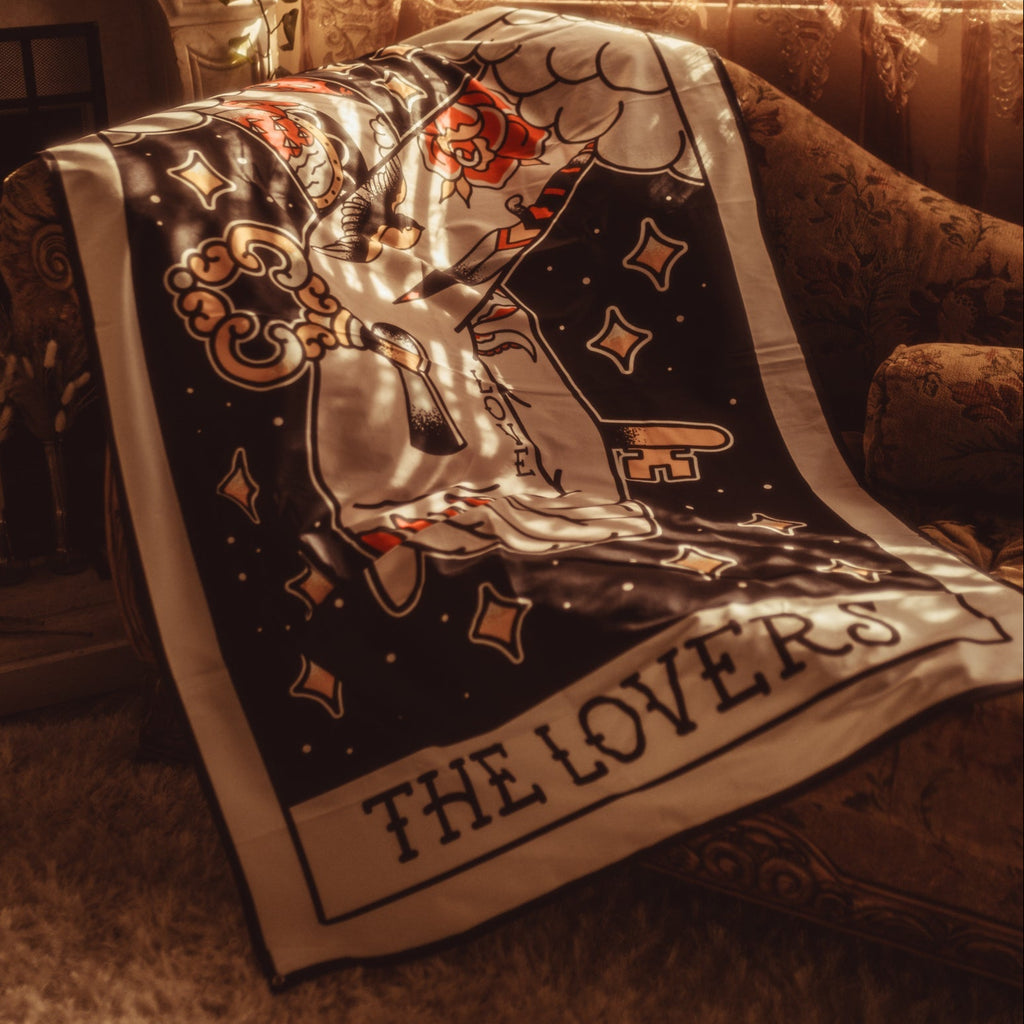 Tarot card design titled 'The Lovers' draped over a chair in a warm, cozy room.