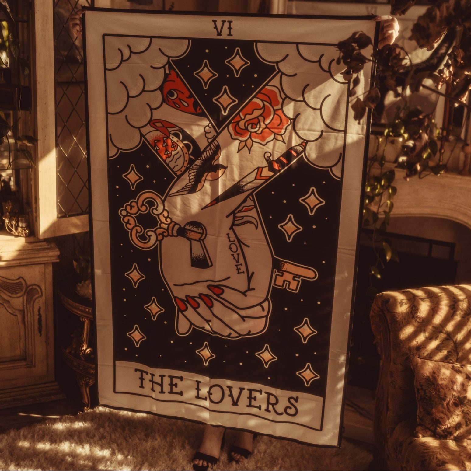 Tarot card titled 'The Lovers' held by a hand with a key, in a warm interior setting.