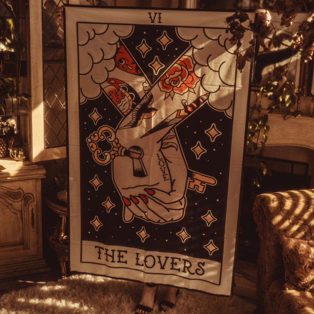 Tarot card titled 'The Lovers' held by a person in a warm, indoor setting.