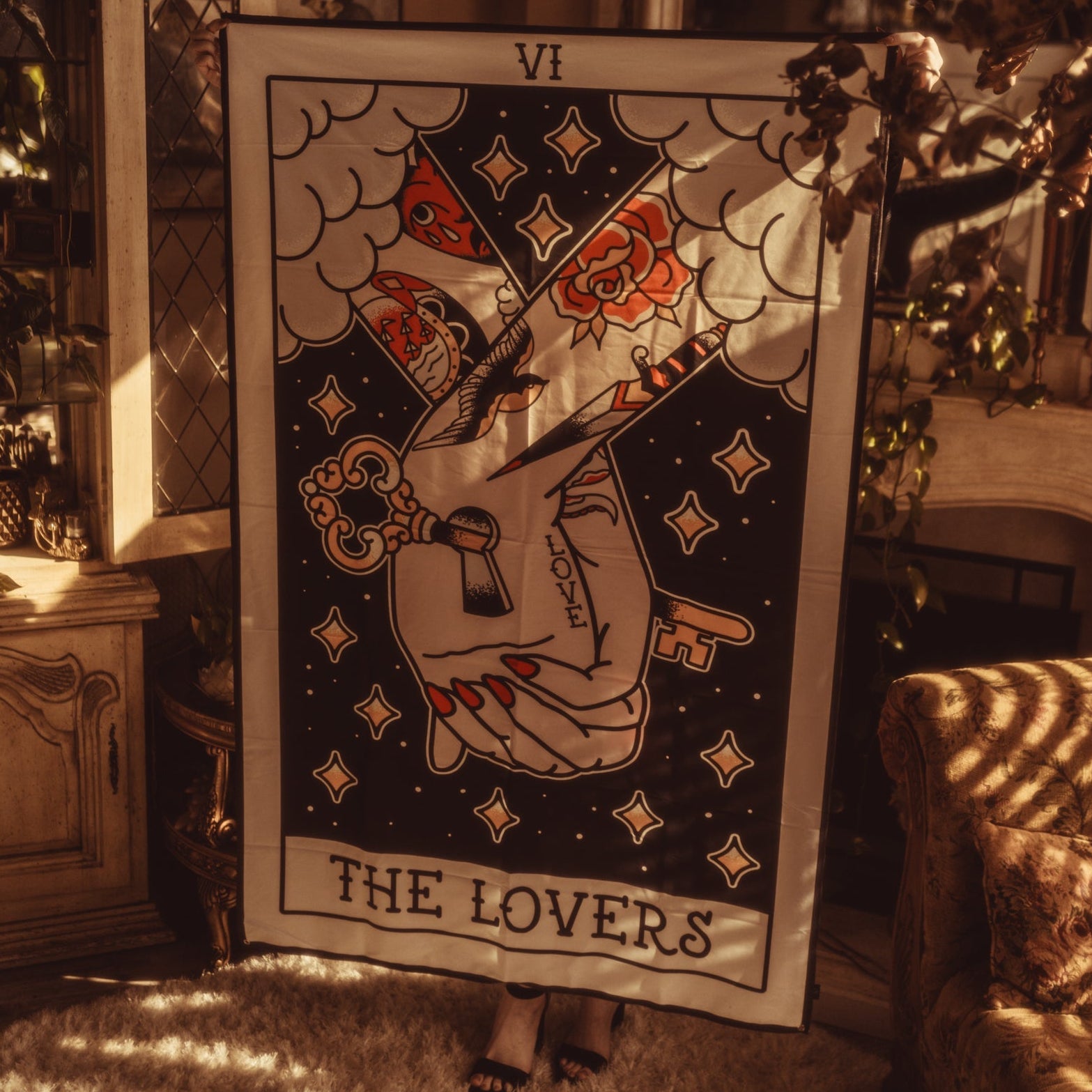Tarot card titled 'The Lovers' held by a person in a warm, indoor setting.