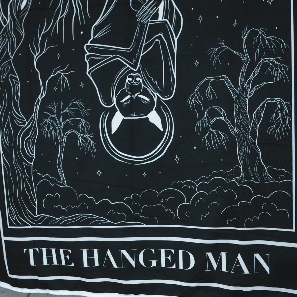 Black and white illustration of 'The Hanged Man' tarot card with trees and night sky.