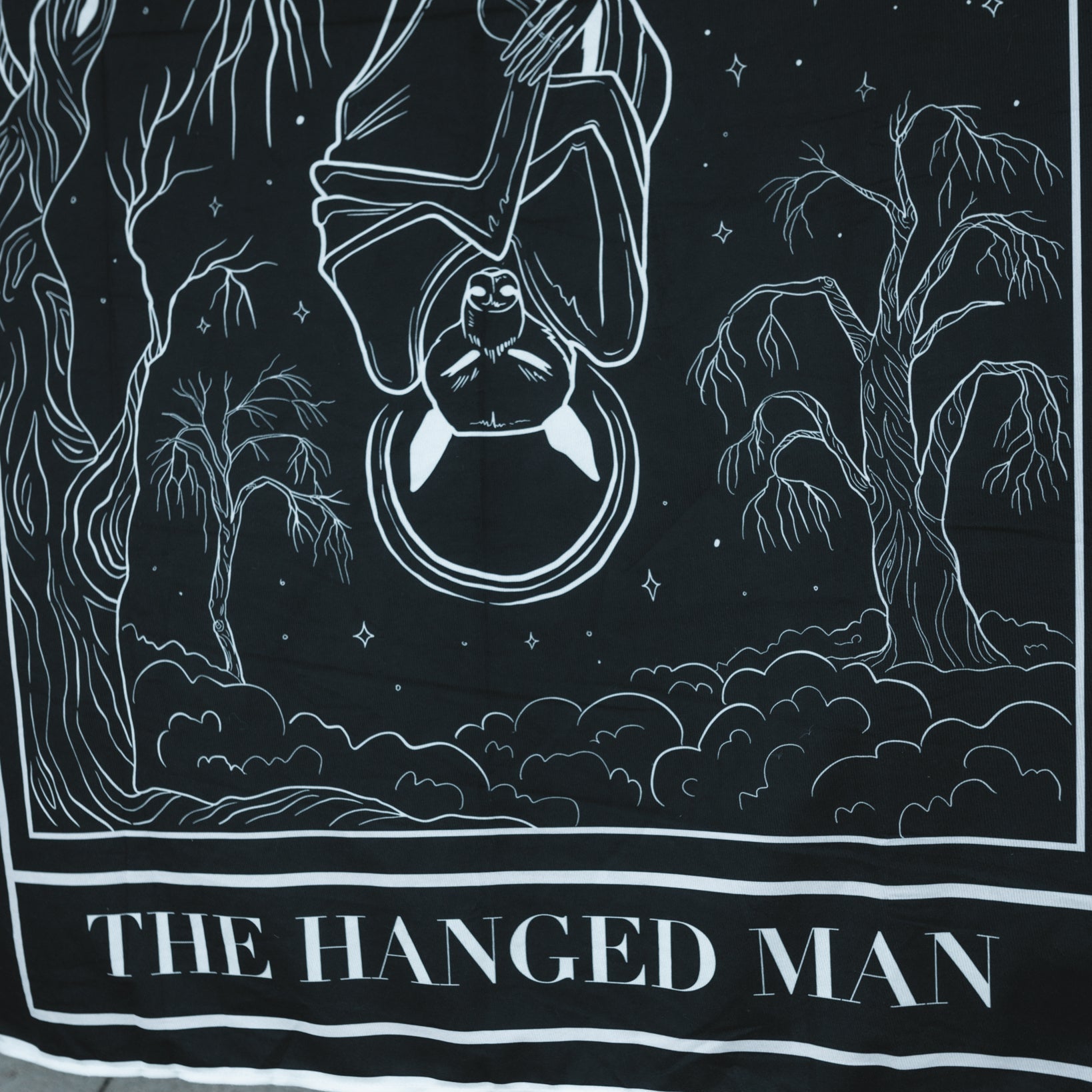 Black and white illustration of 'The Hanged Man' tarot card with trees and night sky.