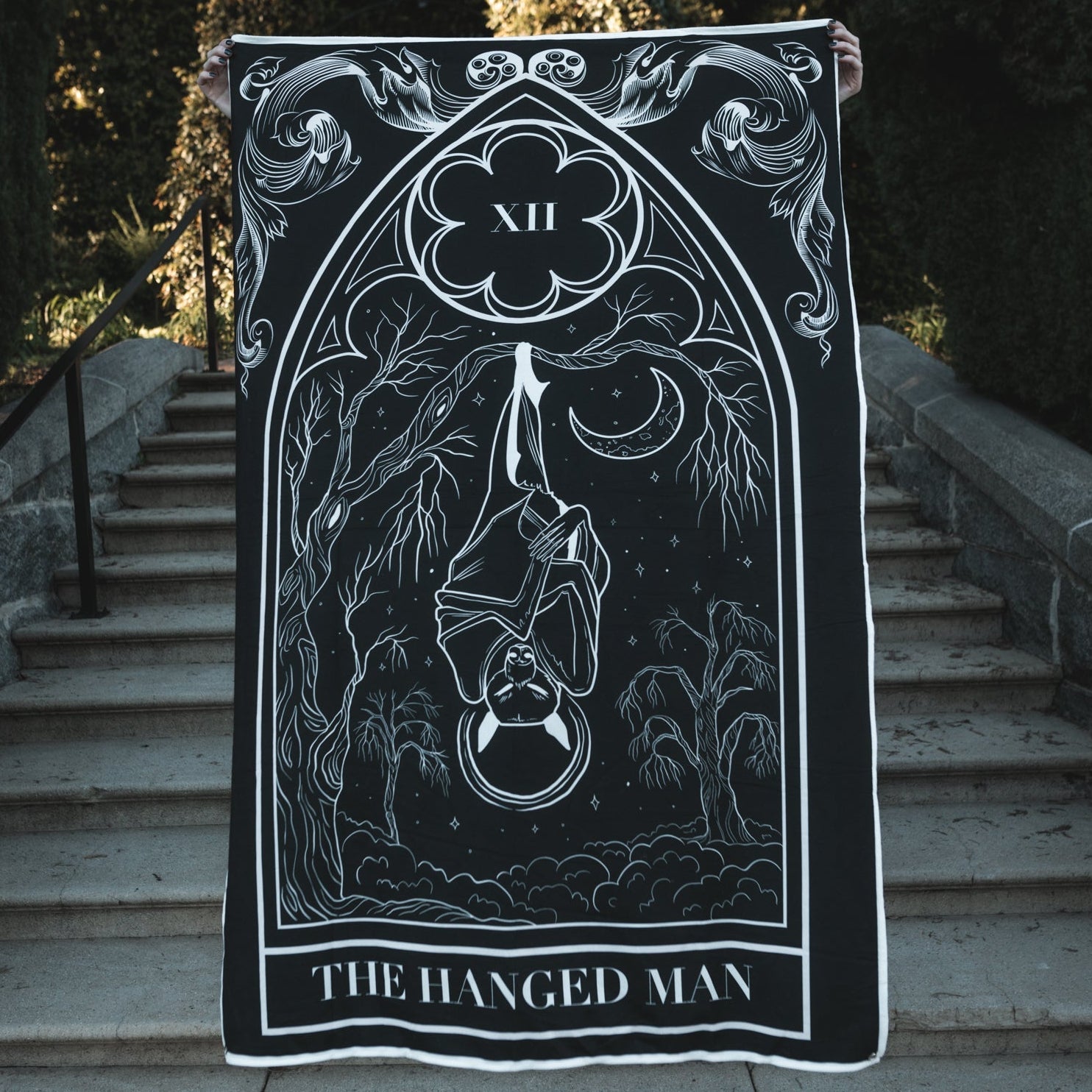 Tarot card featuring 'The Hanged Man' on a black background held up outdoors.