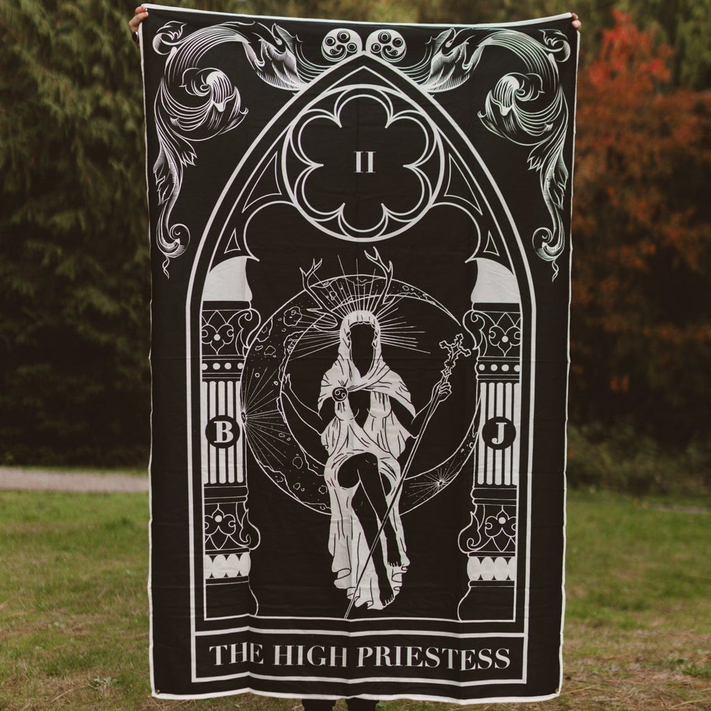 Person holding a tarot card-themed blanket with 'The High Priestess' design outdoors.