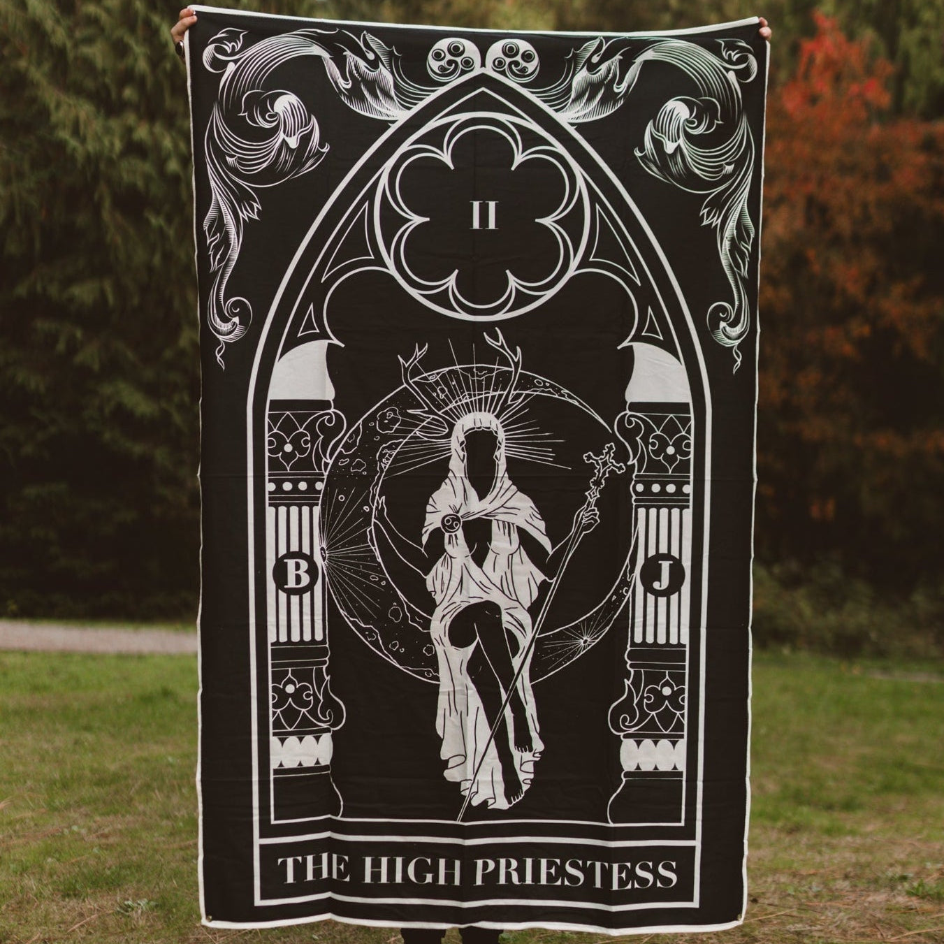 Person holding a tarot card-themed blanket with 'The High Priestess' design outdoors.