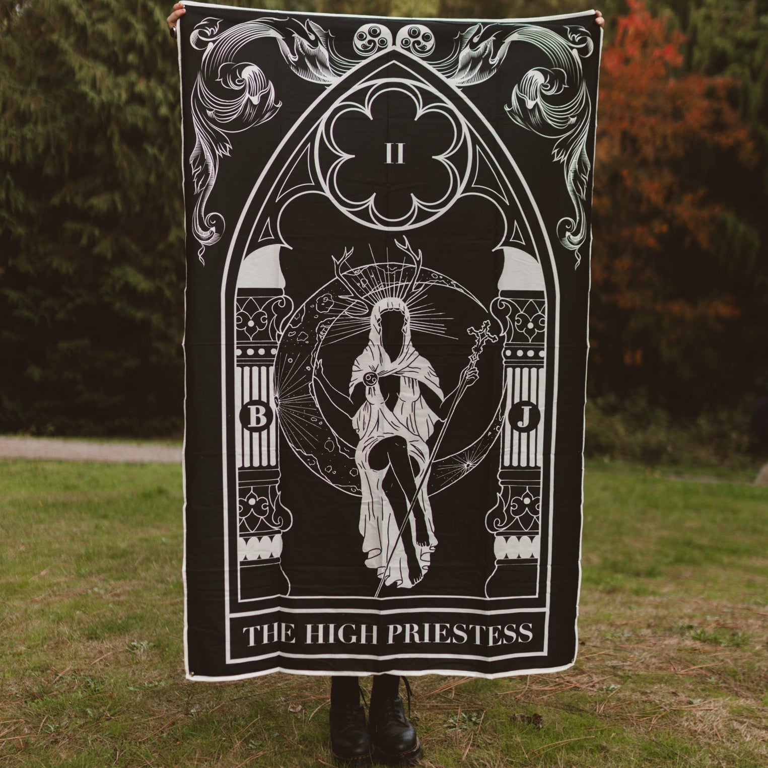 Person holding a tarot card-themed blanket with 'The High Priestess' design outdoors.