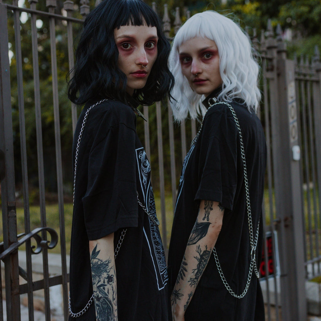 Two individuals with black and white wigs standing in front of a metal gate.