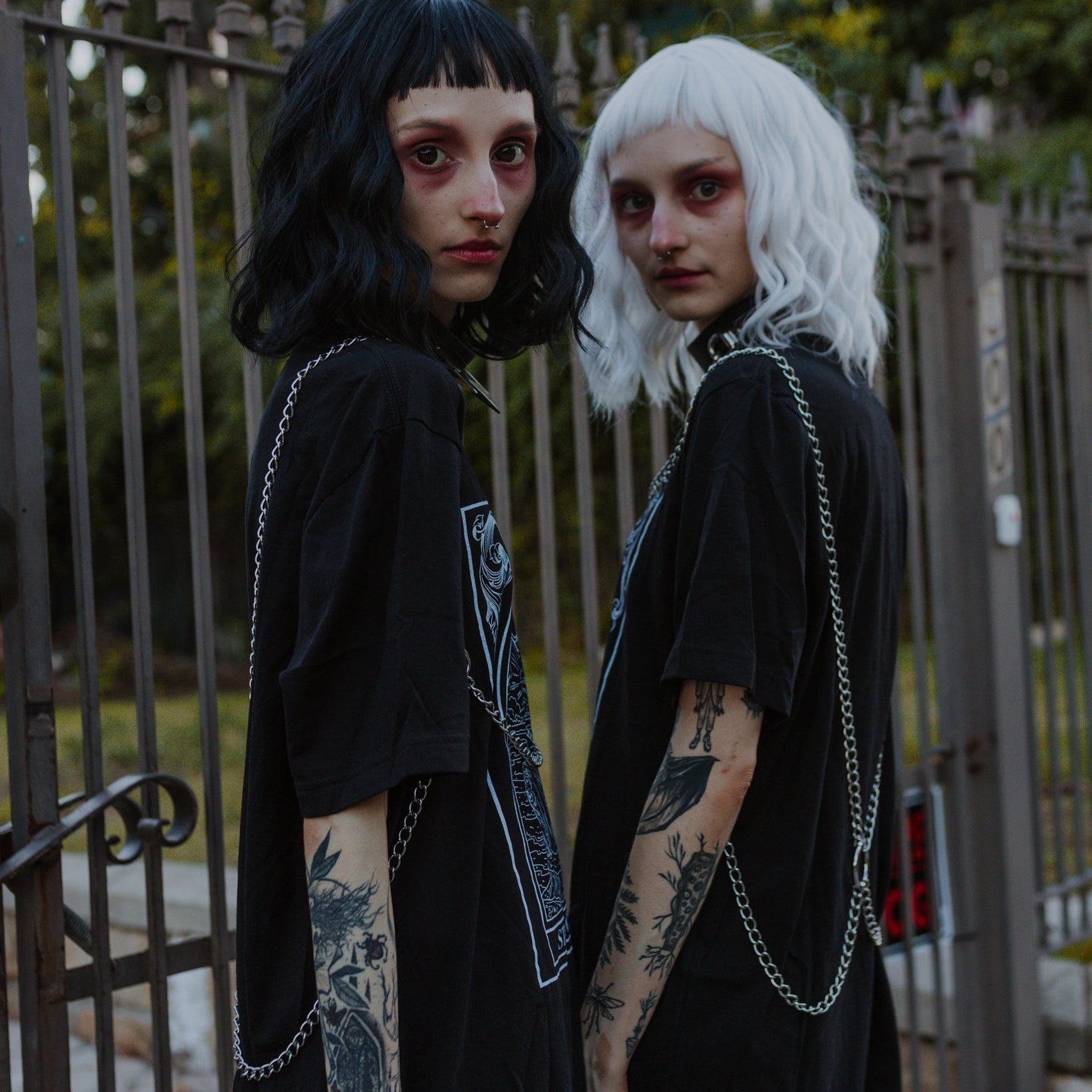 Two individuals with black and white wigs standing in front of a metal gate.