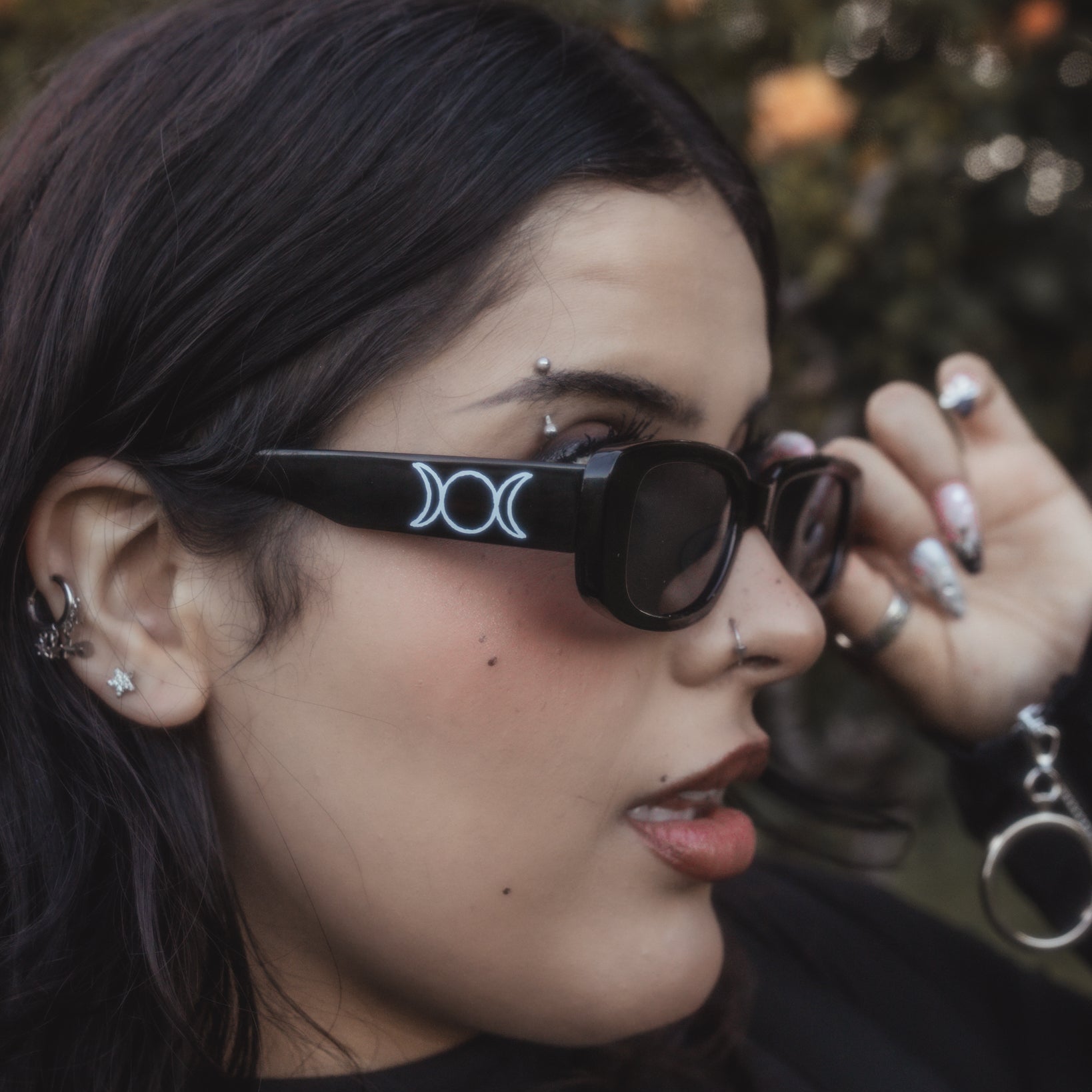 Person wearing black sunglasses with a distinctive logo, outdoors.