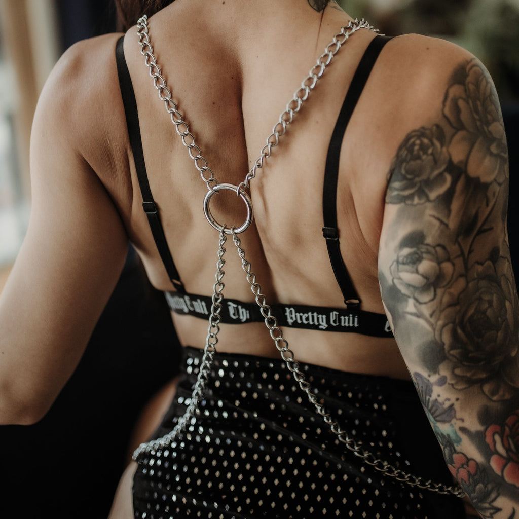Person wearing a black strappy top with chain details and studded pants, showcasing tattoos.