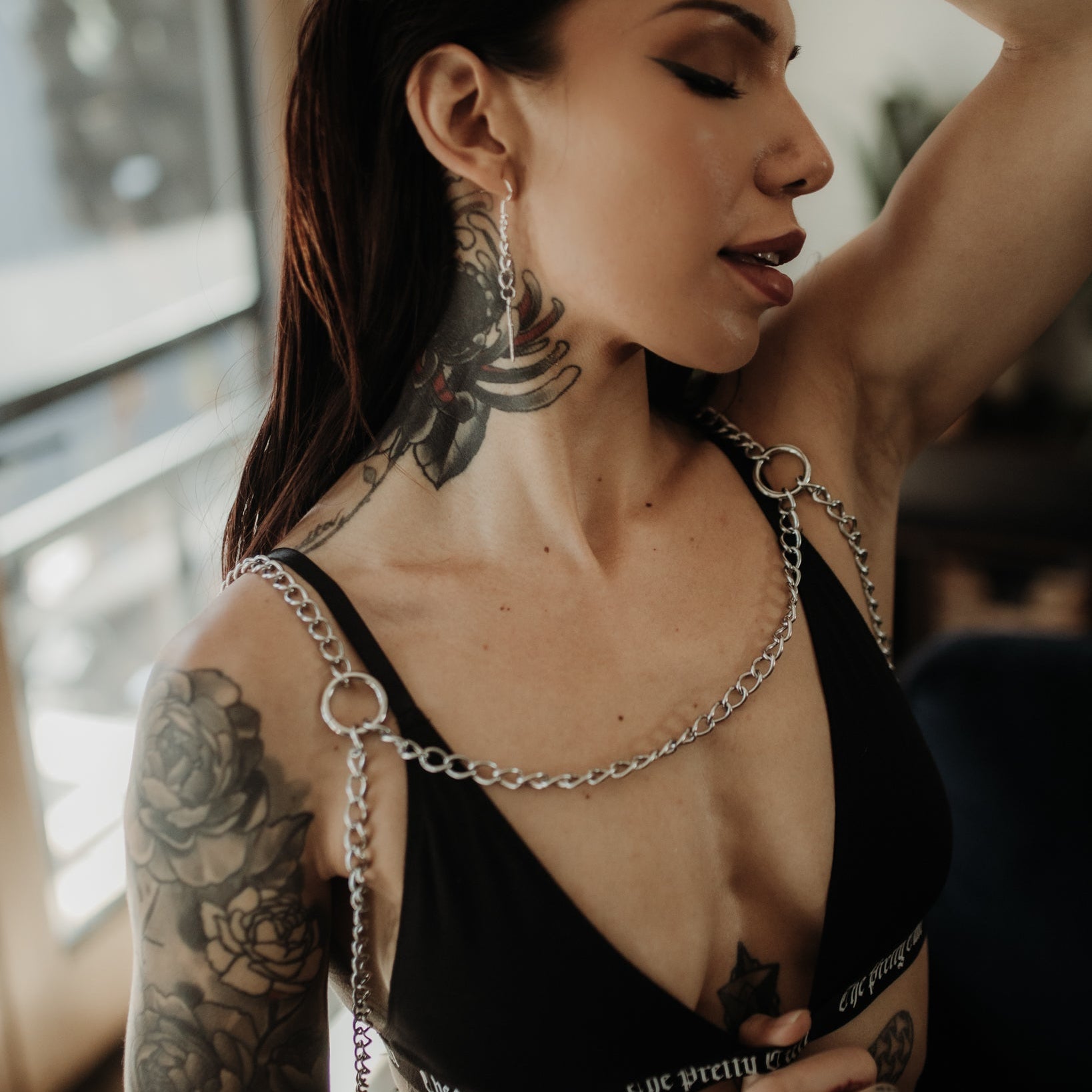 Woman with tattoos wearing a black top with chain straps indoors.