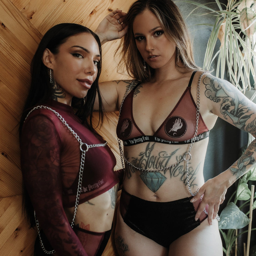 Two women posing together against a wooden wall with tattoos visible.