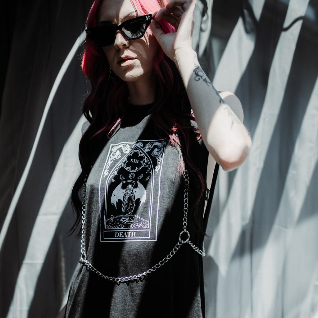 Person wearing a black t-shirt with a graphic design, standing against a wall with shadows.