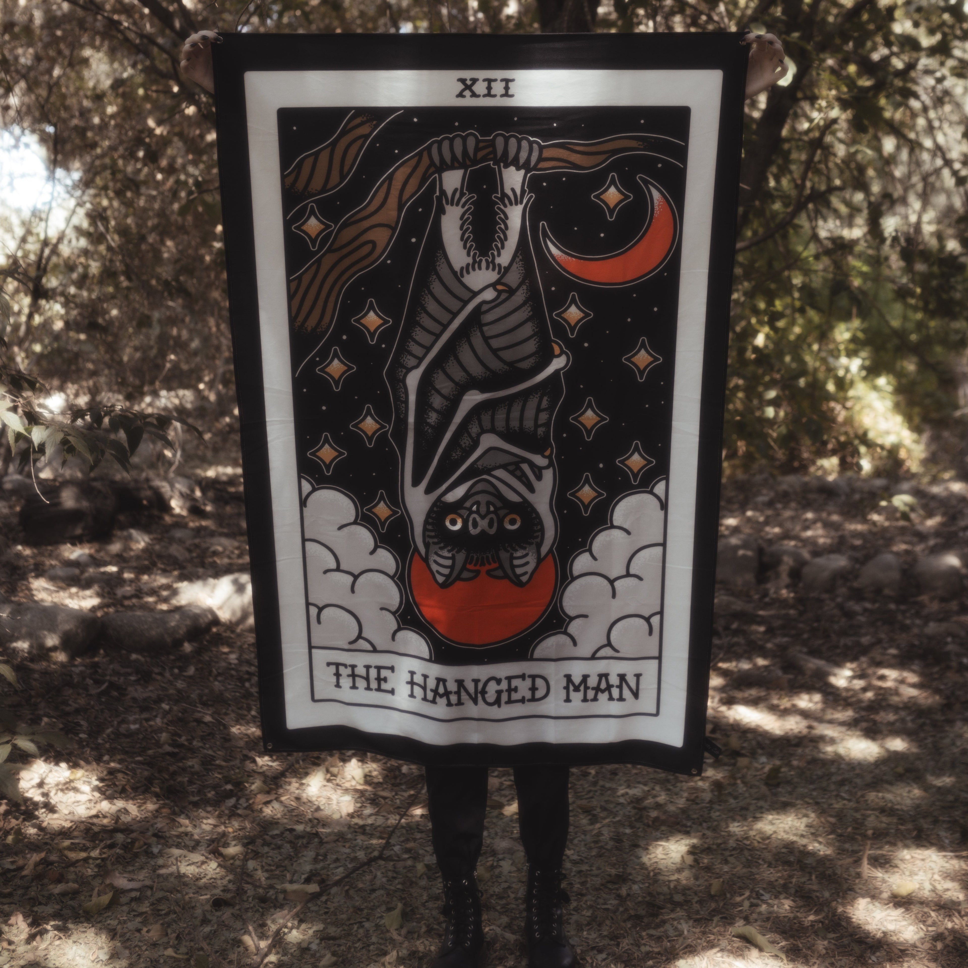 Person holding a tarot card titled 'The Hanged Man' in a forest setting