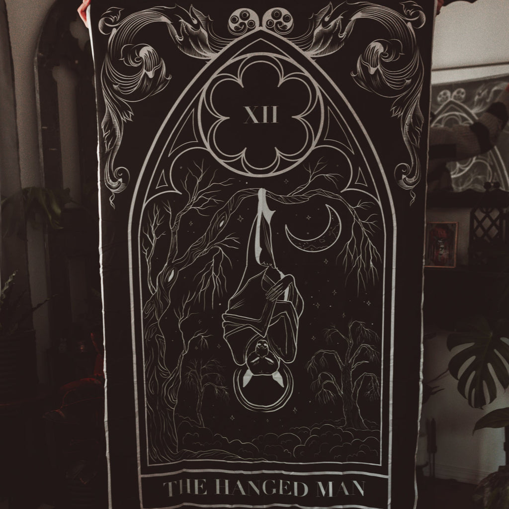 Tarot card featuring 'The Hanged Man' with a bat design, held against a dark background.