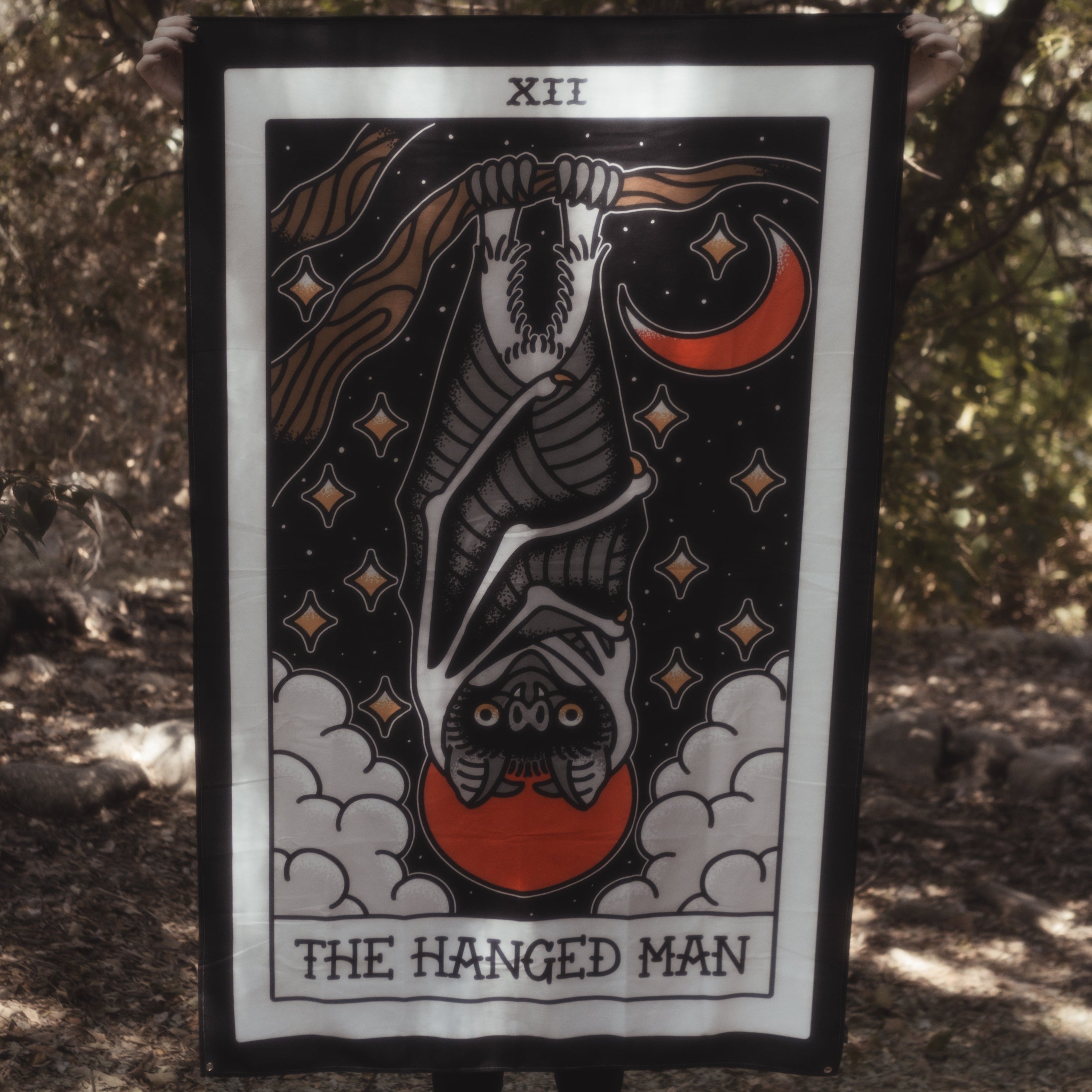 Person holding a tarot card titled 'The Hanged Man' in a forest setting