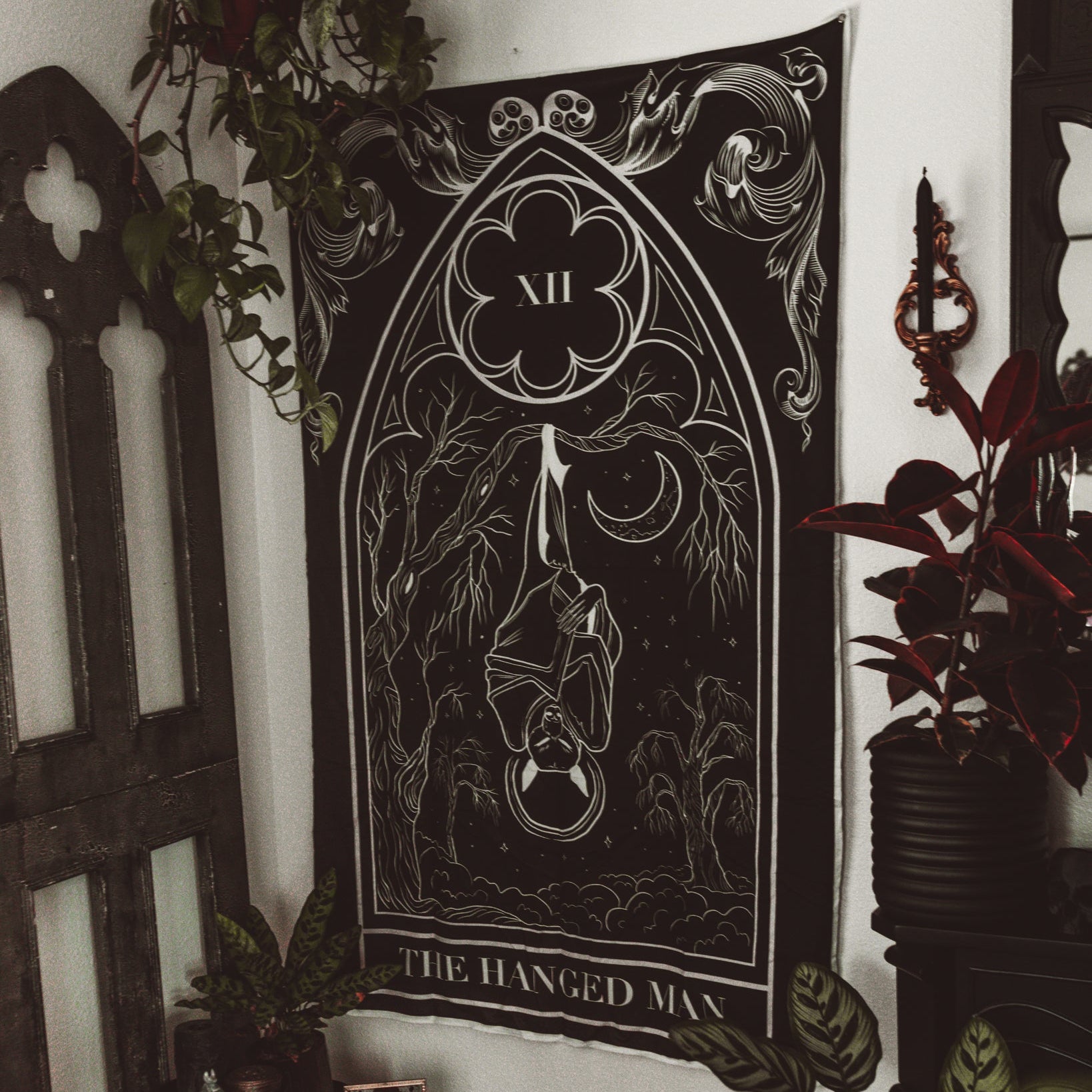 Tapestry of 'The Hanged Man' from a tarot card series hanging on a wall with decorative elements.