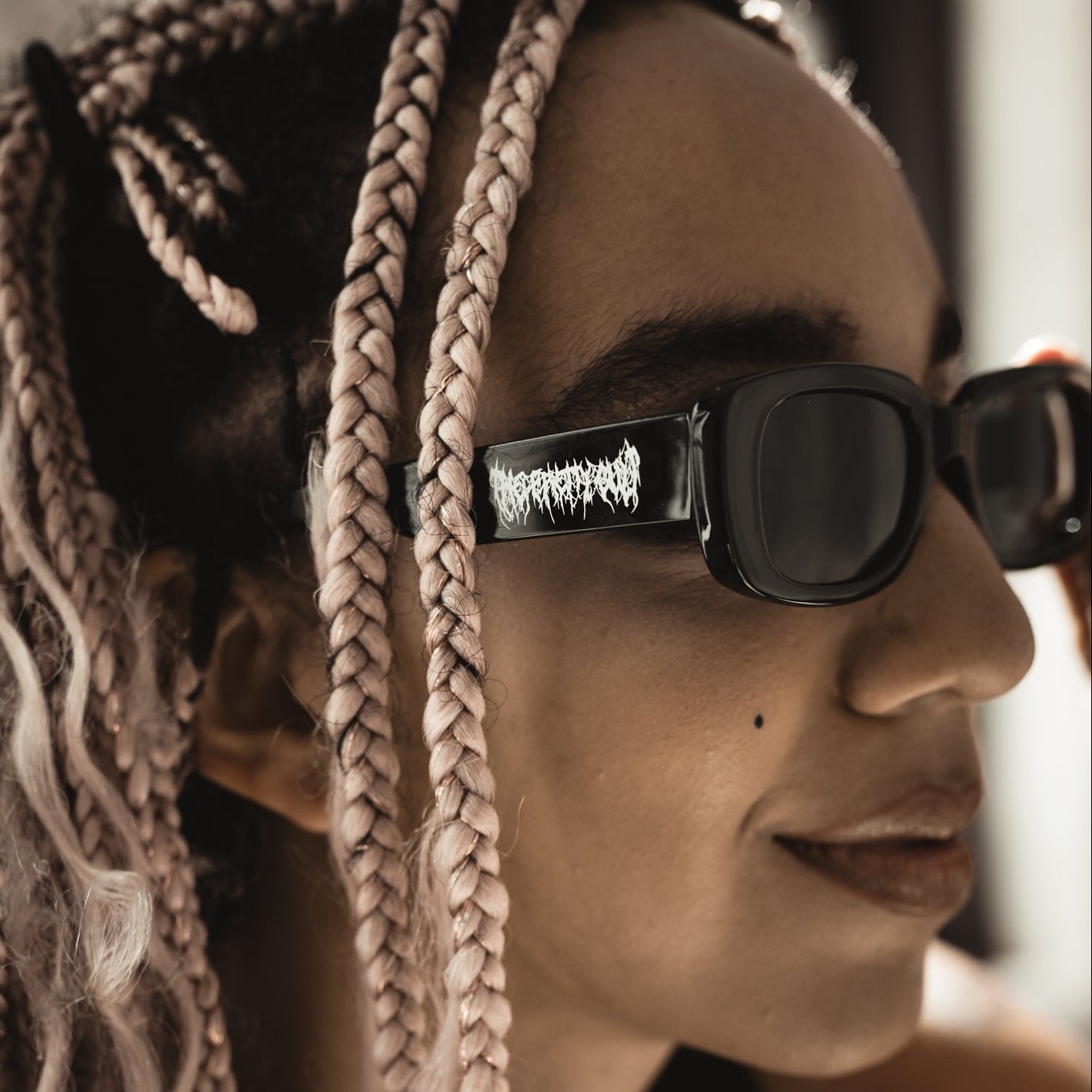 Person with braided hair wearing dark sunglasses with a visible brand logo.