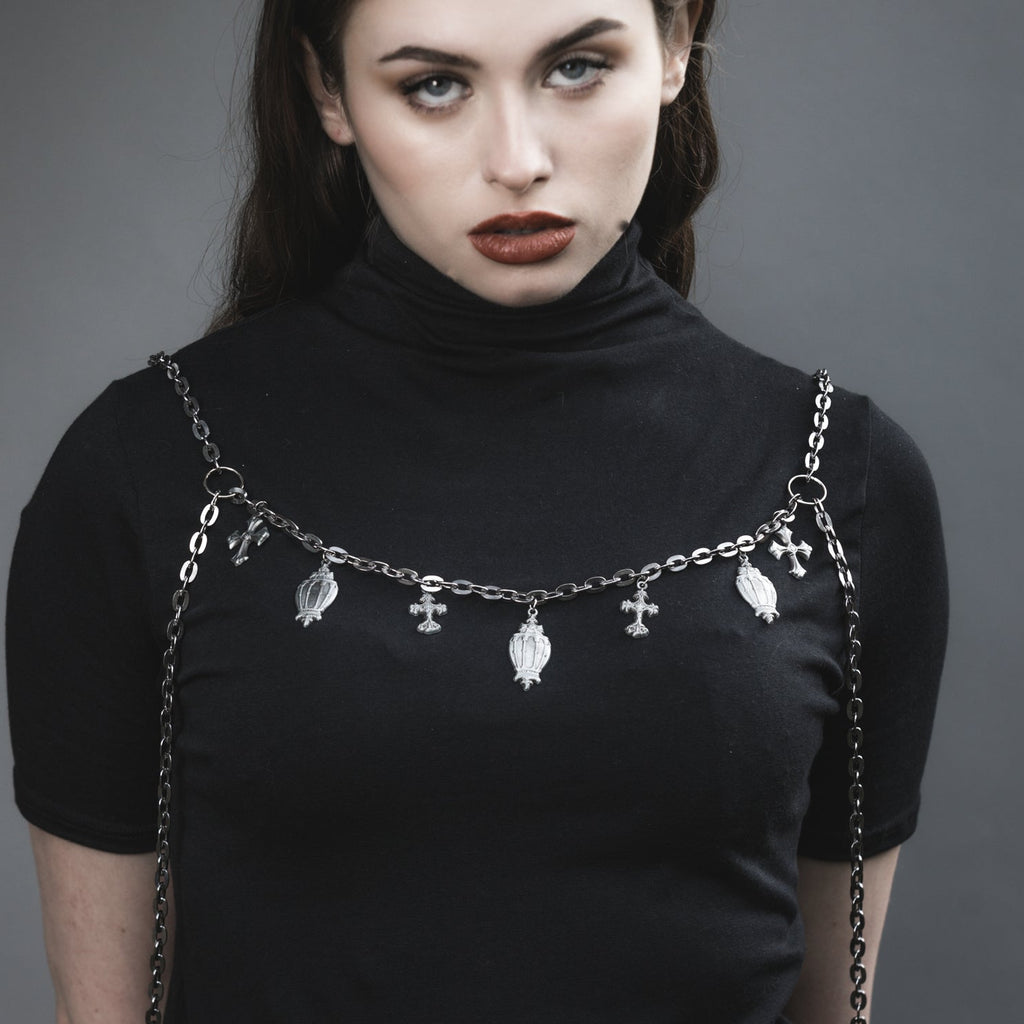Woman wearing a black turtleneck with a chain strap over shoulders against a gray background