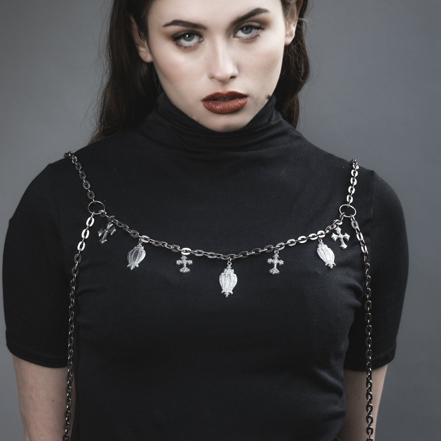 Woman wearing a black turtleneck with a chain strap over shoulders against a gray background