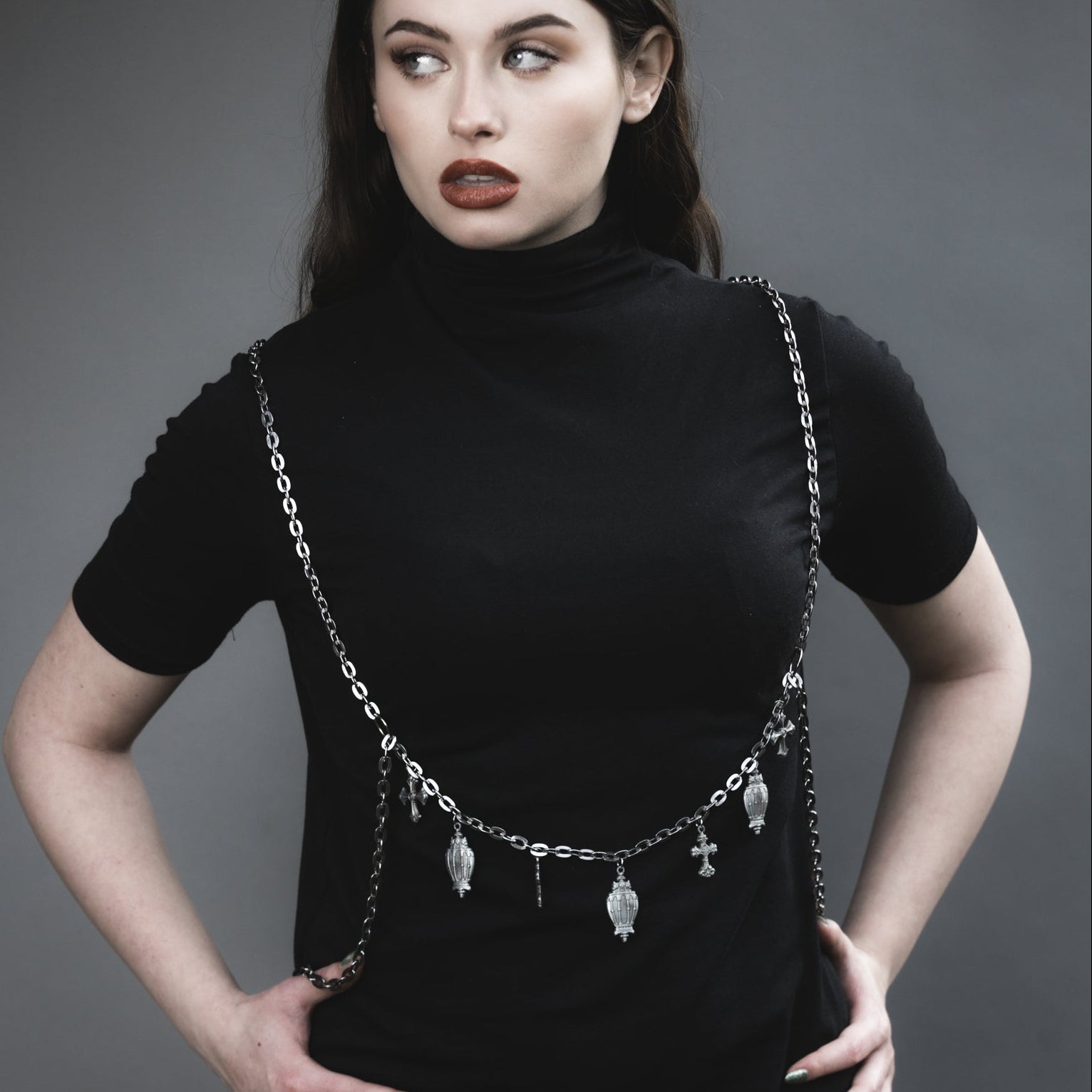 Woman wearing a black turtleneck with a chain accessory against a gray background