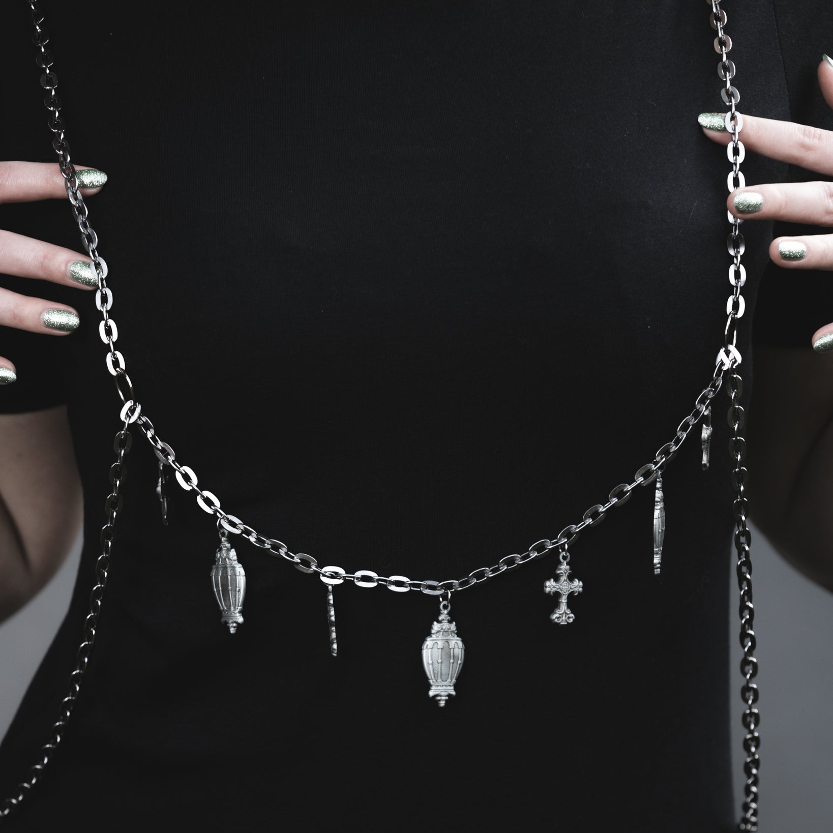 Necklace with chain and small pendants held by a person against a black background