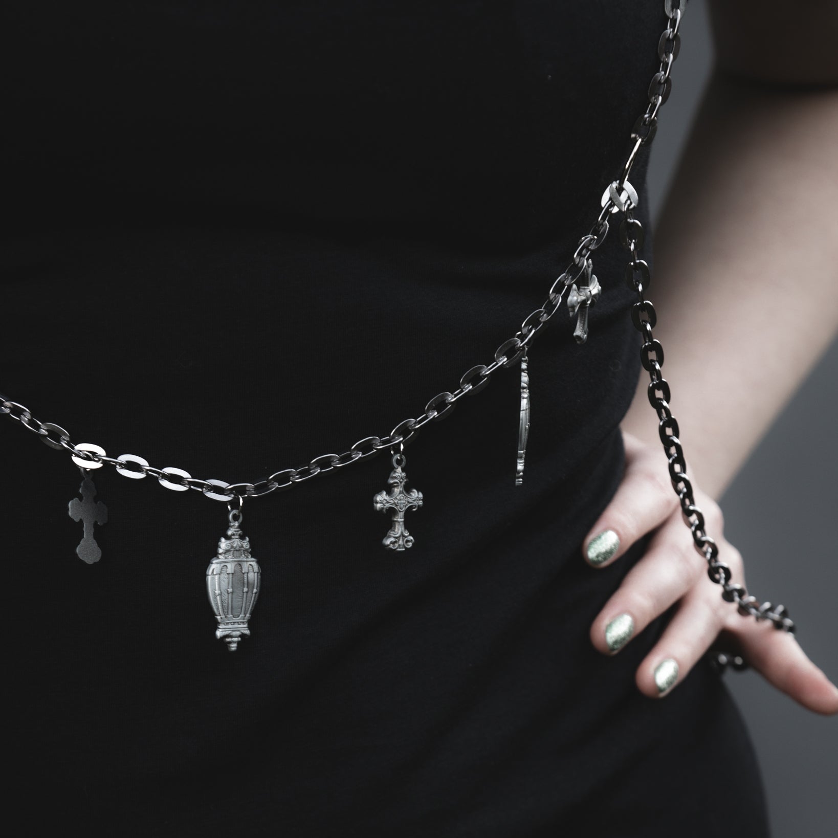 Person wearing a black dress with a silver chain belt featuring charms against a dark background