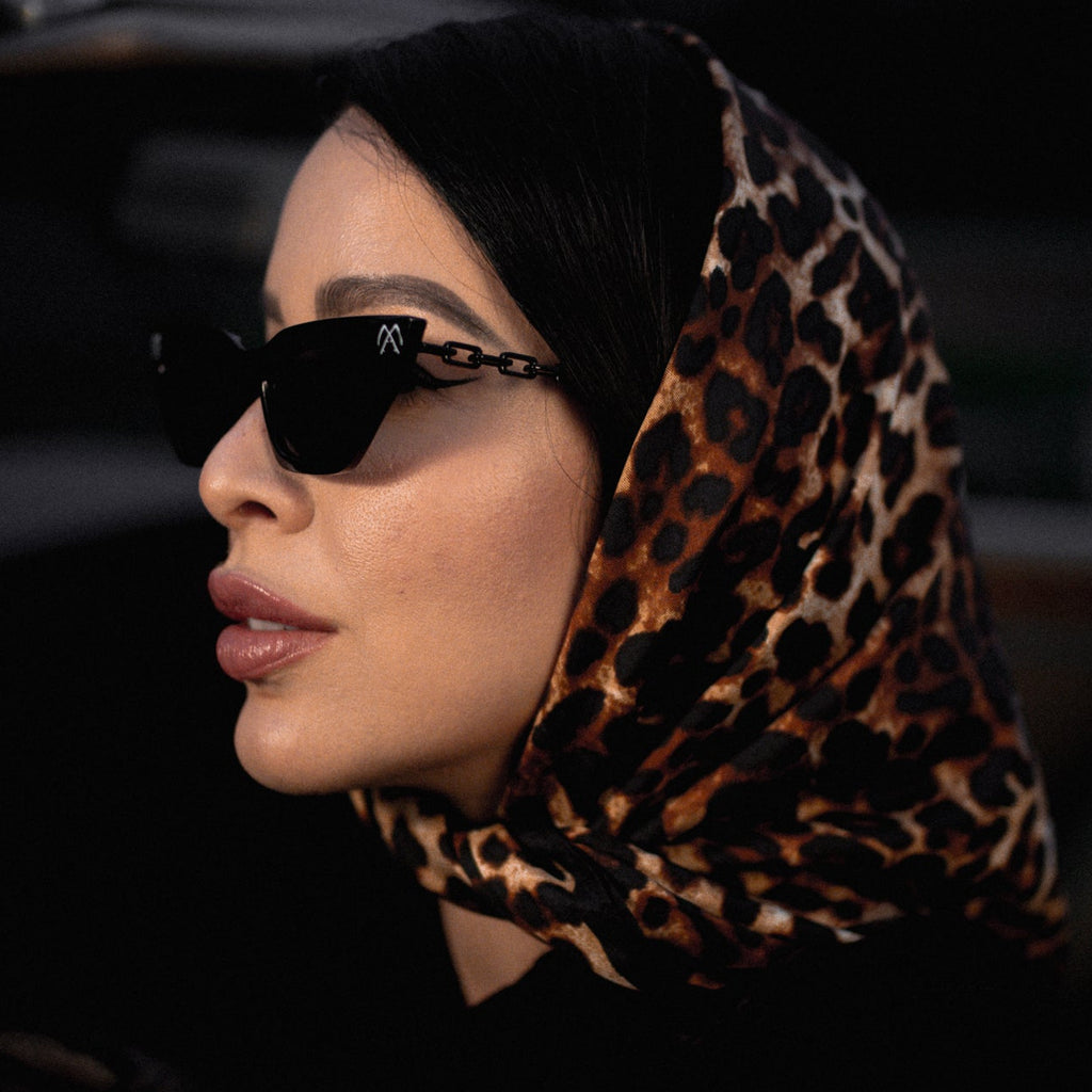 Woman wearing a leopard print hijab and sunglasses, sitting inside a vehicle.
