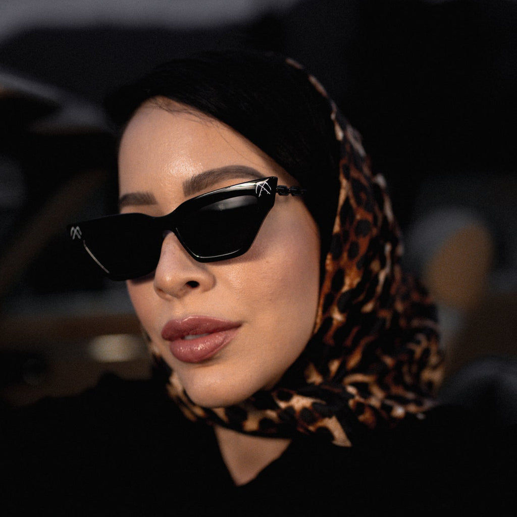 Woman wearing sunglasses and a leopard print hijab peeking out from a car.