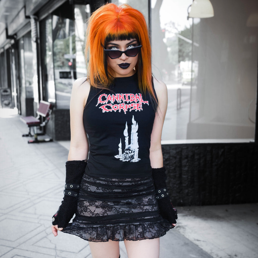 Person with orange hair wearing a black tank top with graphic design and a black skirt on a city street.