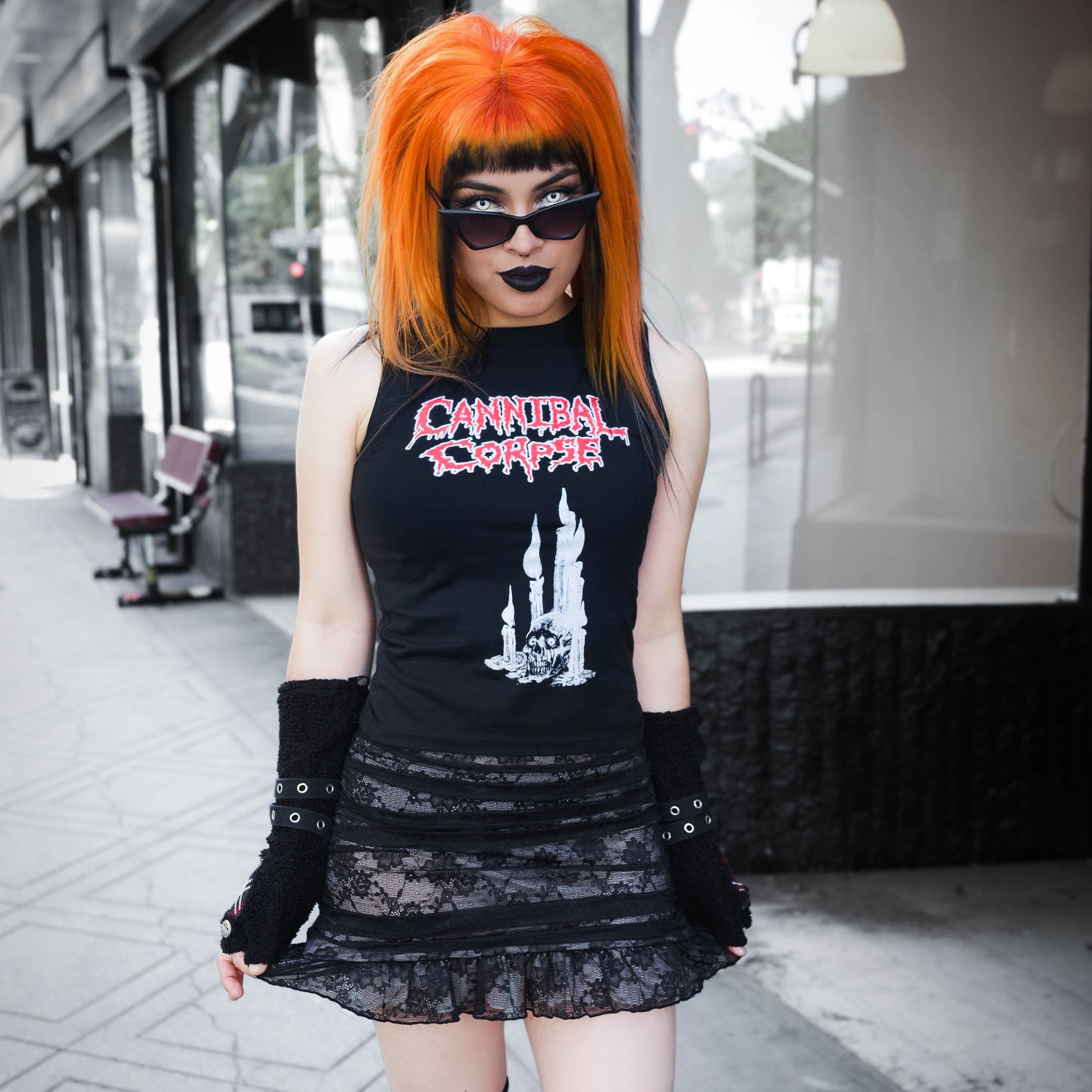 Person with orange hair wearing a black tank top with graphic design and a black skirt on a city street.