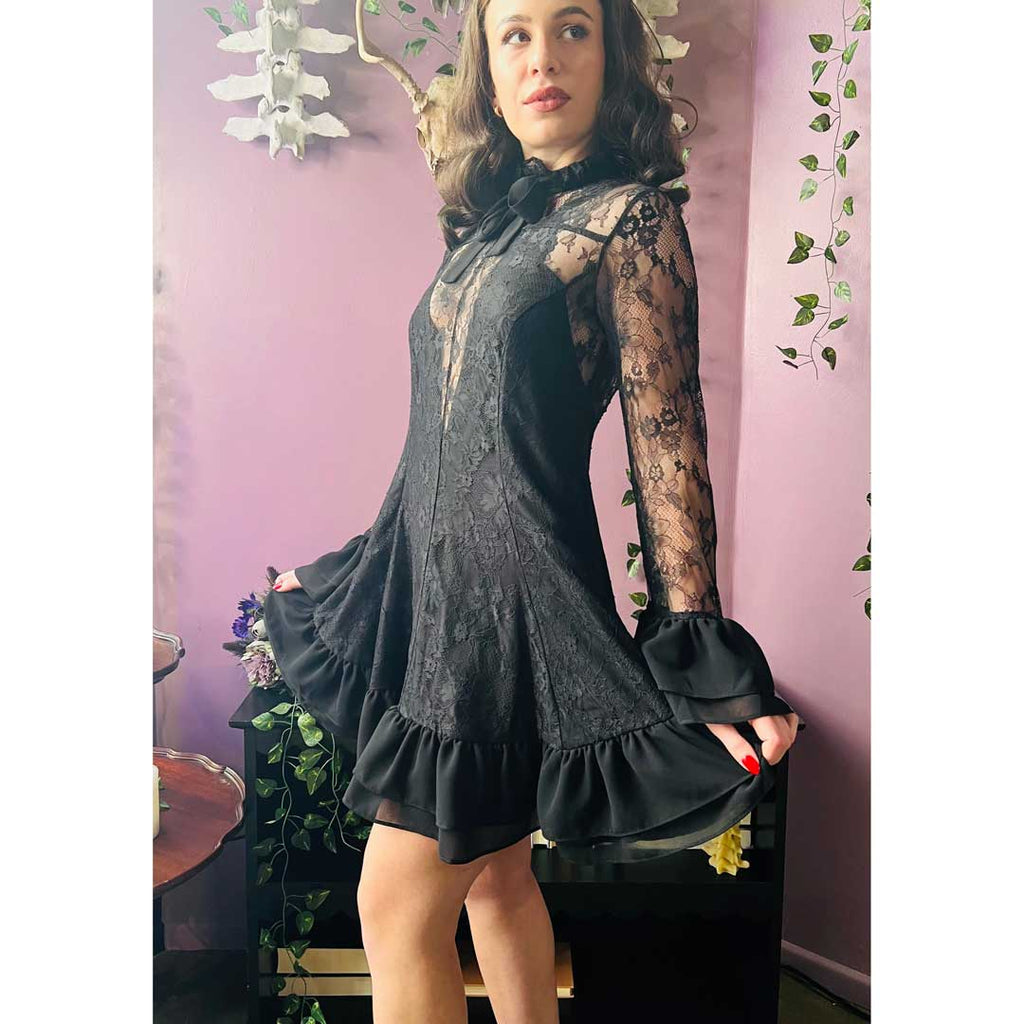 Woman wearing a black dress with lace sleeves in a room with pink walls and plants.