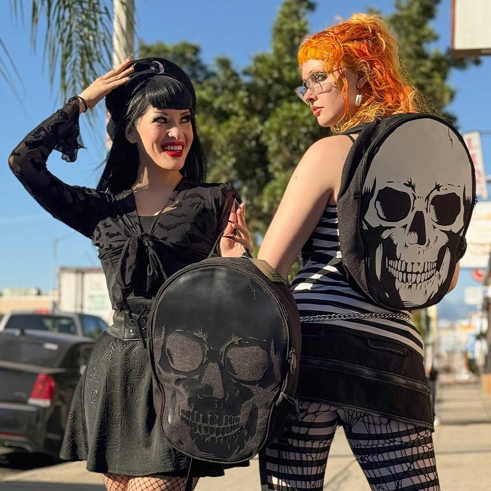 Two women with unique hairstyles holding skull-shaped bags on a street.