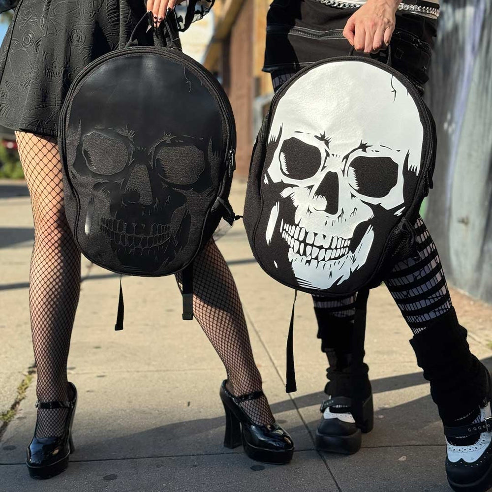 Two people wearing black backpacks with skull designs on a sidewalk.