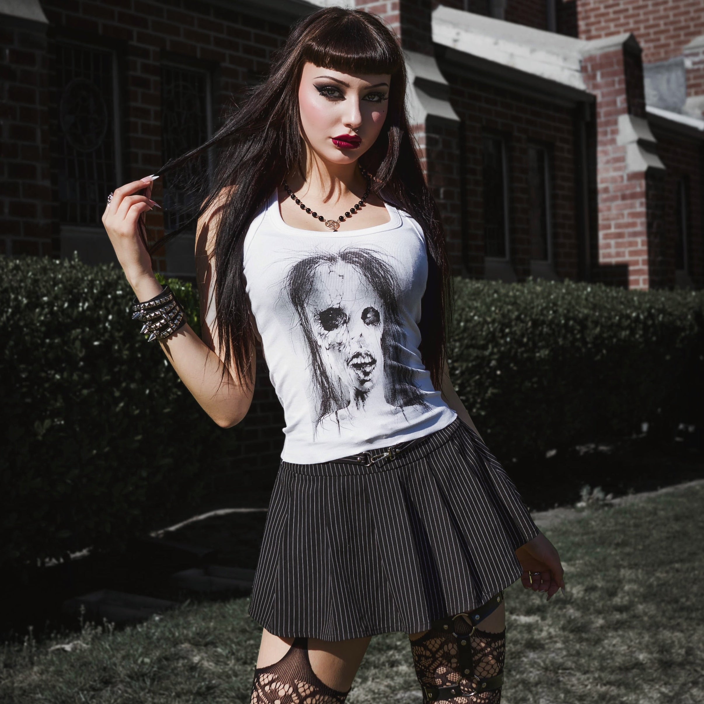 Woman wearing a white t-shirt with a graphic design, black skirt, and lace stockings outdoors.