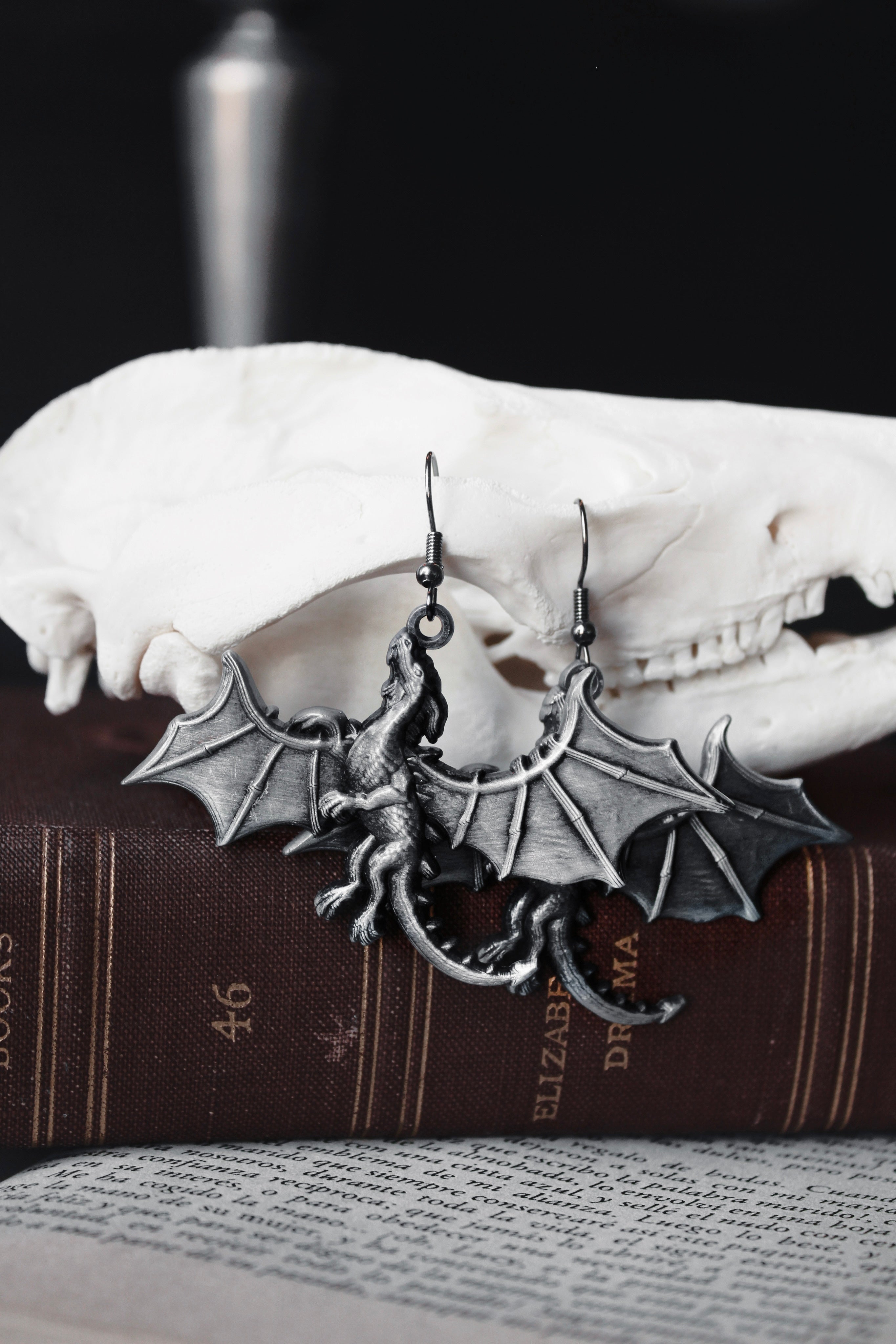 Silver bat-shaped earrings on a skull with a book in the background