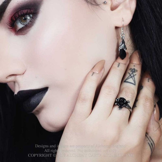 Close-up of a person wearing a black rose ring and feather earring with dark makeup.