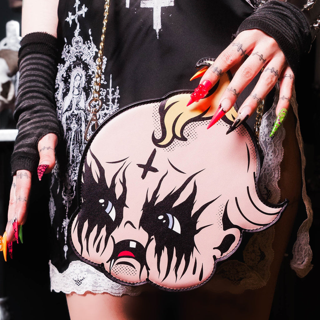 Person wearing a black outfit with white designs, holding a pink and black bag with a face design.