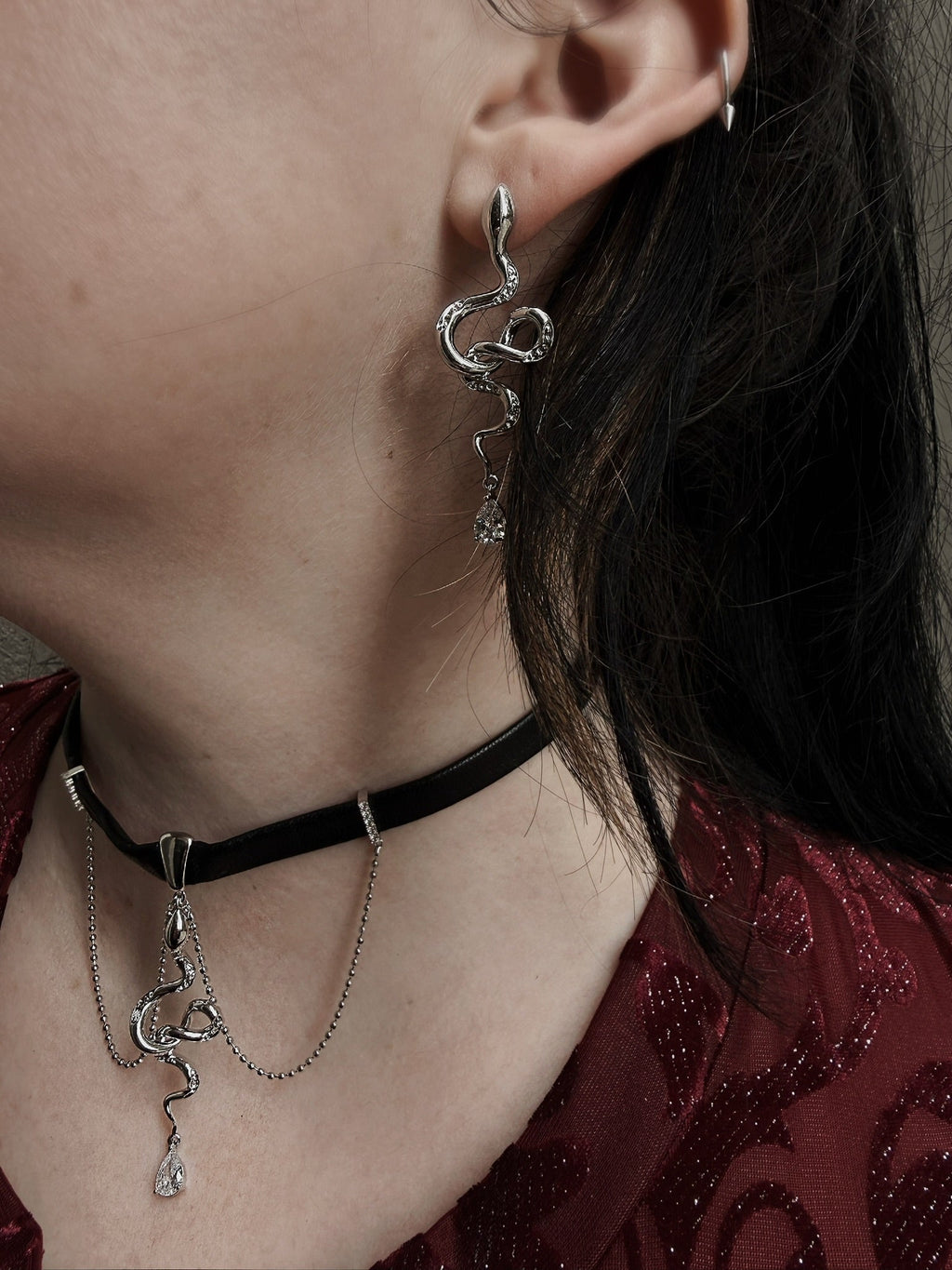 Close-up of a person wearing silver earrings and a black choker with intricate designs.