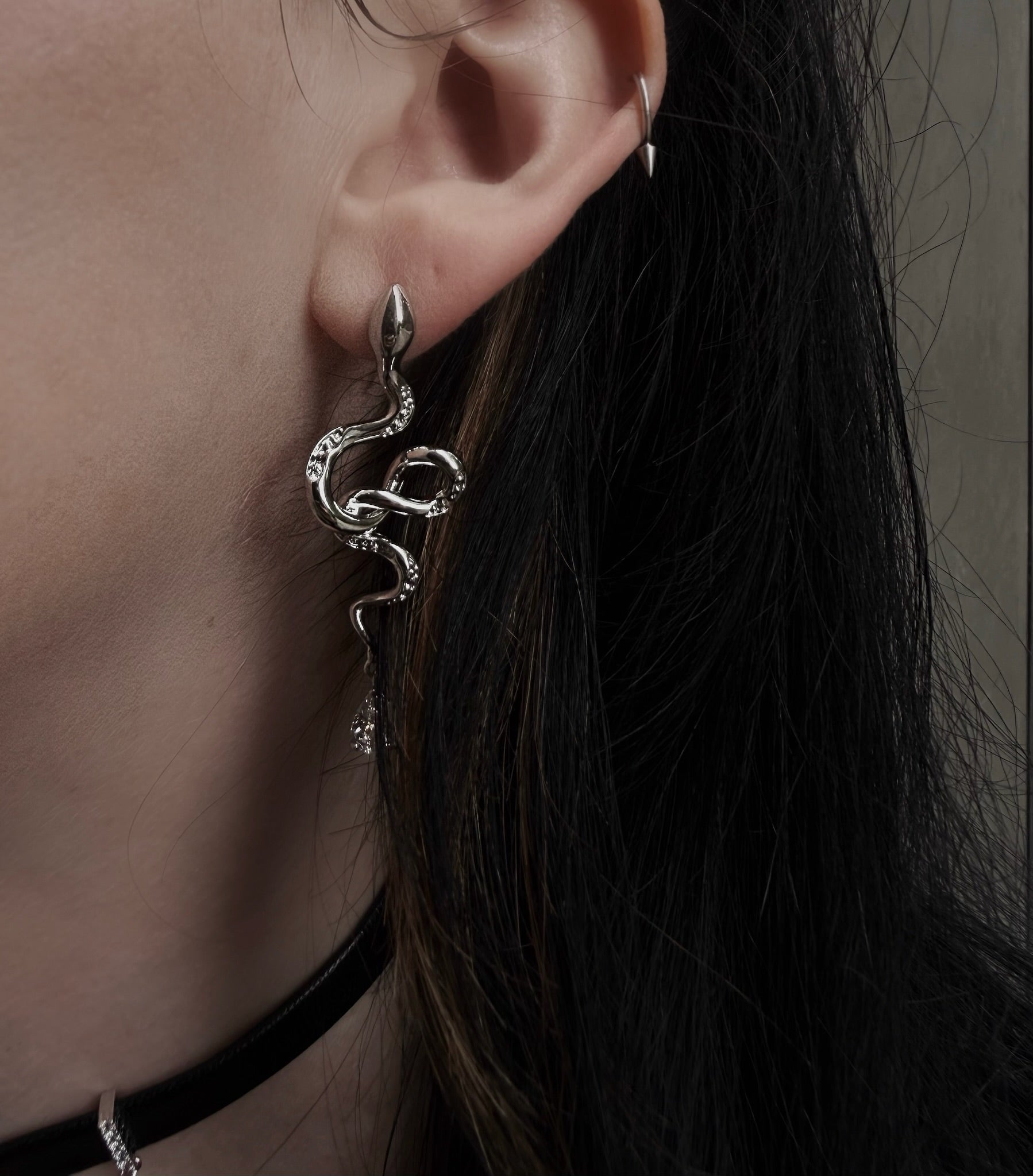 Close-up of an ear wearing a silver earring with dark hair and blurred background