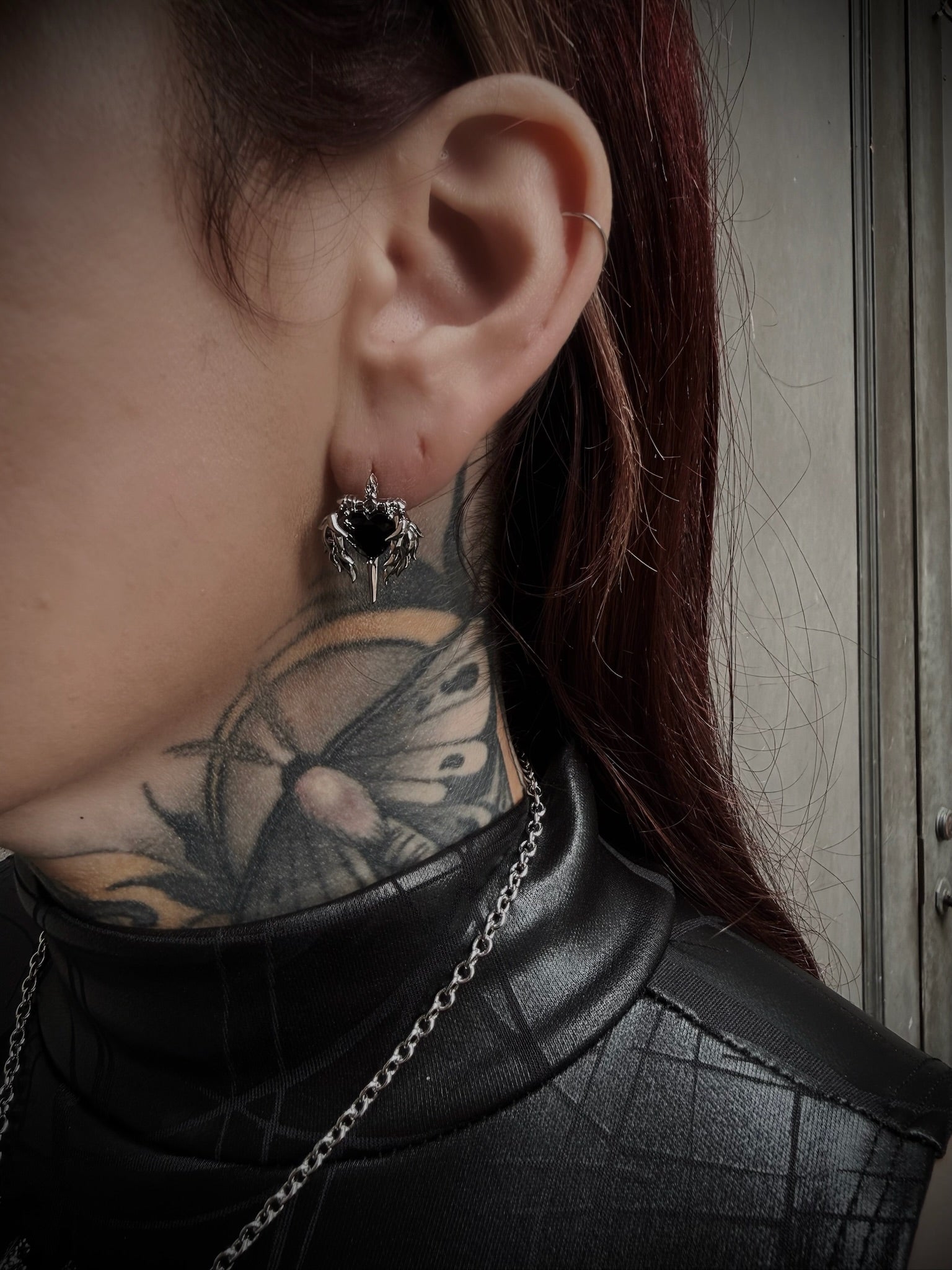 Close-up of an ear with a black earring, tattooed neck, and black turtleneck.