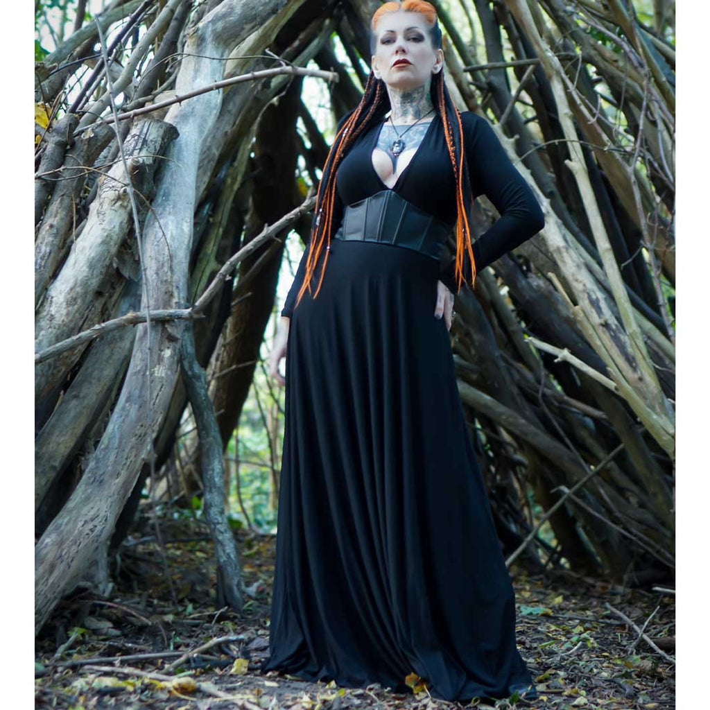 Person in a black dress standing in a forest setting with wooden logs.