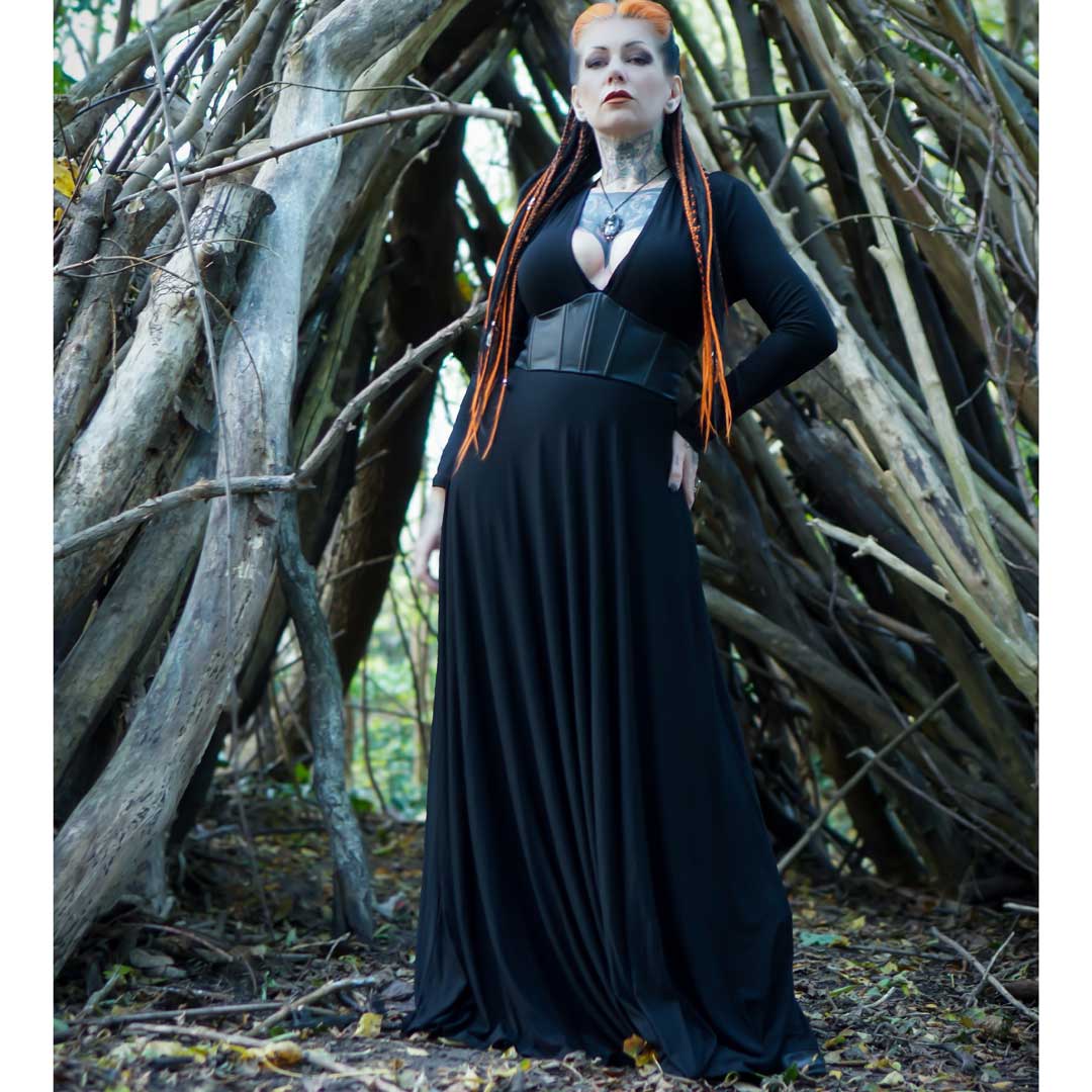 Person in a black dress standing in a forest setting with wooden logs.