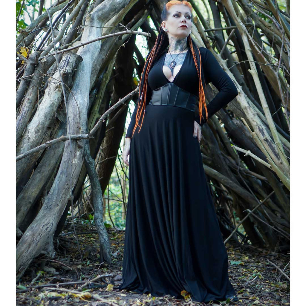 Woman in a black dress standing in front of a wooden structure in a forest