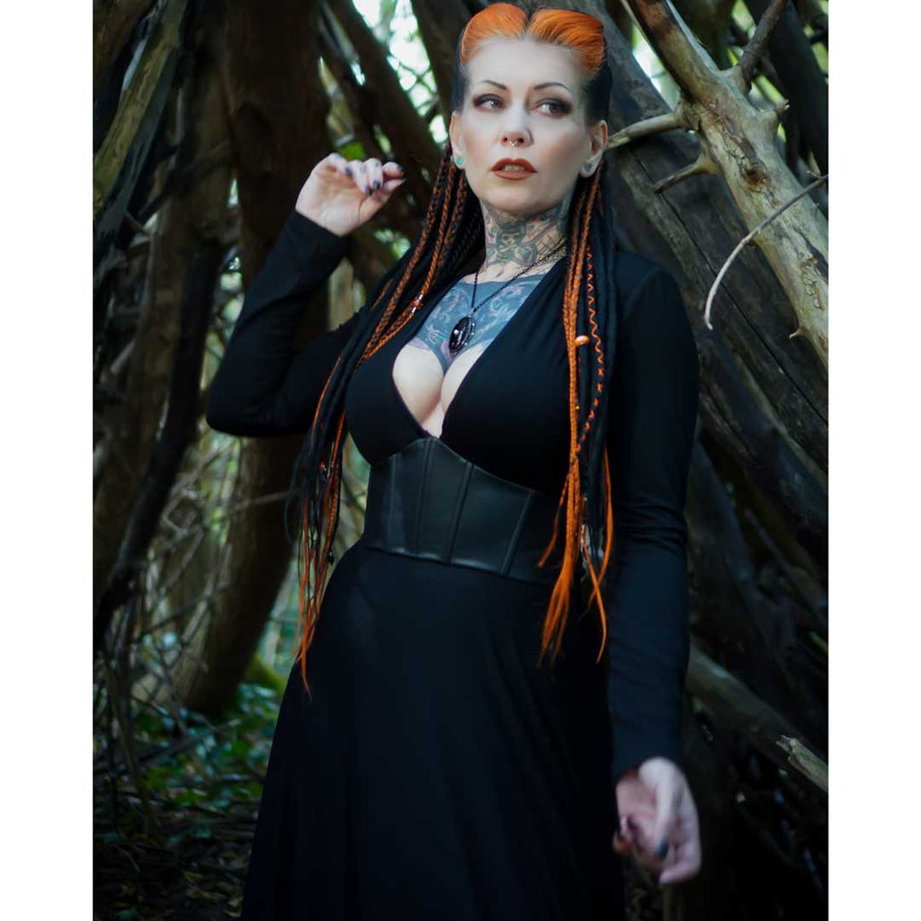 Woman in a black outfit with orange hair standing in a forest setting