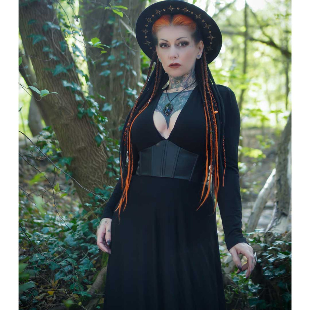 Woman in a black dress and hat with orange hair standing in a forest