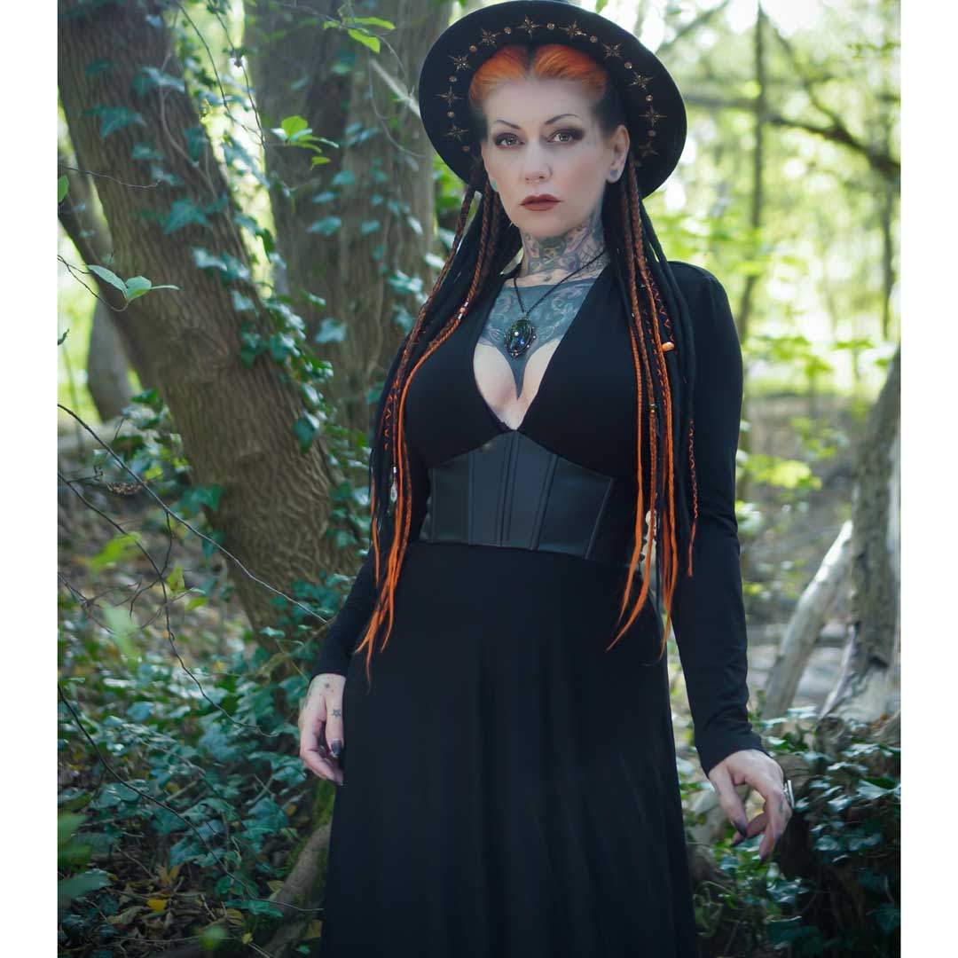 Woman in a black dress and hat with orange hair standing in a forest