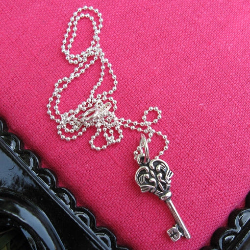 Silver key-shaped pendant necklace on a pink background